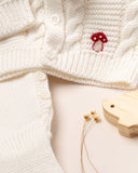 Na imagem, vemos detalhes do sofisticado bordado exclusivo de cogumelo vermelho no casaquinho na cor off white.