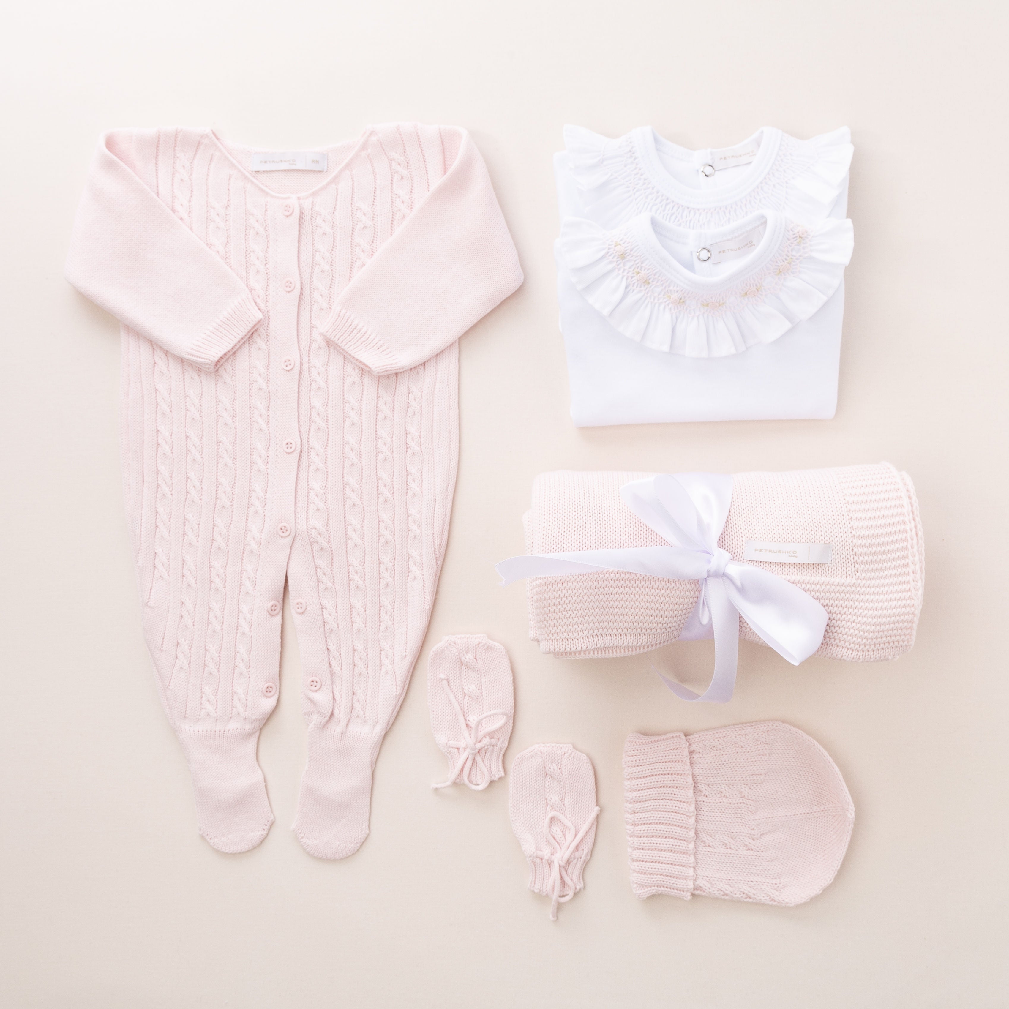 Na foto vemos a saída de maternidade rosa que é uma opção exclusiva para mamães que procuram uma roupa de qualidade e delicadeza para suas bebês. As peças são antialérgicas, macias e possuem bordados personalizados feitos à mão. Na foto, é possível ver o kit completo composto por 6 peças: macacão, 2 bodies, manta, gorro e luvinha. Cada peça é embalada com cuidado em uma caixa de presente especial para tornar esse momento ainda mais inesquecível. Todos os detalhes são únicos e feitos com amor.
