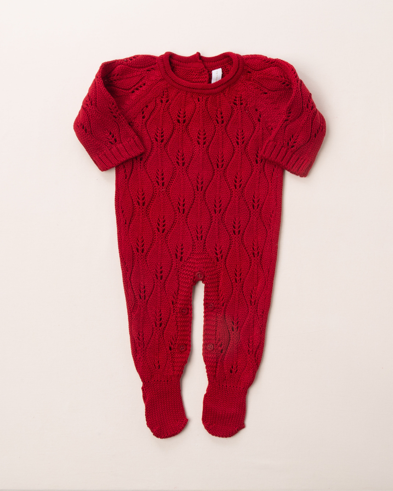 O macacão em tricô vermelho é encantador, com uma trama delicada que chama a atenção. Ele é prático para a troca da bebê, com abotoamento nas entrepernas e costas, facilitando a troca sem perder o charme.