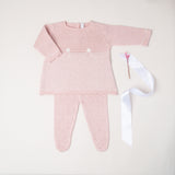 Na imagem, é possível ver o conjunto Helena em tricô na cor rosa, composto por duas peças: blusa, calça. As peças são confeccionadas com tecidos de alta qualidade para garantir suavidade e conforto à recém-nascida.