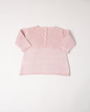 Na imagem, é possível ver as costas da blusa em tricô rosa com um delicado trabalho na trama, que traz charme e elegância para a peça. Possui abertura com botões para facilitar a troca da roupa.