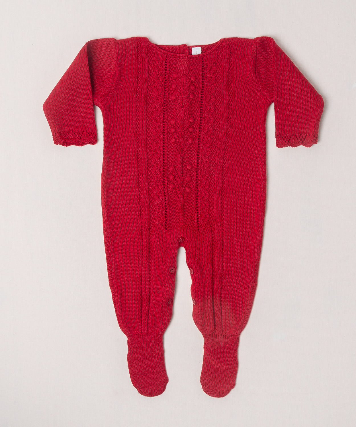 O macacão em tricô vermelho é encantador, com uma trama delicada que chama a atenção. Ele é prático para a troca da bebê, com abotoamento nas entrepernas e costas, facilitando a troca sem perder o charme.