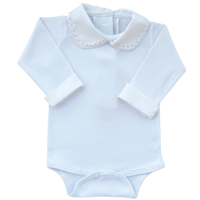 A foto destaca o body 100% algodão com gola bordada à mão e punhos brancos, que é usado por baixo do macacão. O body é uma peça delicada e confortável, complementando o conjunto da bebê.